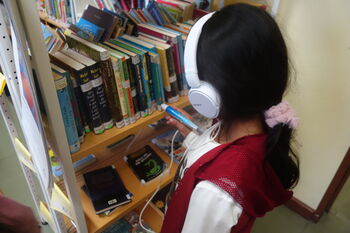 Kind mit Kopfhörern und Stift am Bücherregal Kind mit Kopfhörern und Stift am Bücherregal