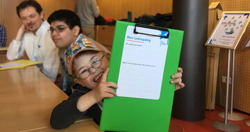 Junge mit Downsyndrom hält fröhlich einen Fragebogen in die Kamera Junge mit Downsyndrom hält fröhlich einen Fragebogen in die Kamera