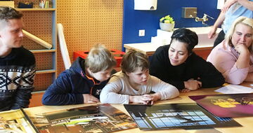 Zwei Schüler*innen betrachten zusammen mit einer Einzellhelferin große Fotos am Tisch Zwei Schüler*innen betrachten zusammen mit einer Einzellhelferin große Fotos am Tisch