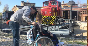 Junge im Rollstuhl und sein Einzelfallhelfer betrachten eine rote Lokomotive auf dem Rangierplatz im Museumshof Junge im Rollstuhl und sein Einzelfallhelfer betrachten eine rote Lokomotive auf dem Rangierplatz im Museumshof